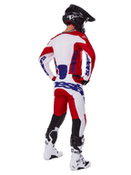 Piloto de motocross visto de costas a usar a camisola e calças Alpinestars 2025 Racer Veil em vermelho e branco, com logótipos azuis, capacete preto e botas brancas, conjunto de equipamento completo para corridas todo-o-terreno