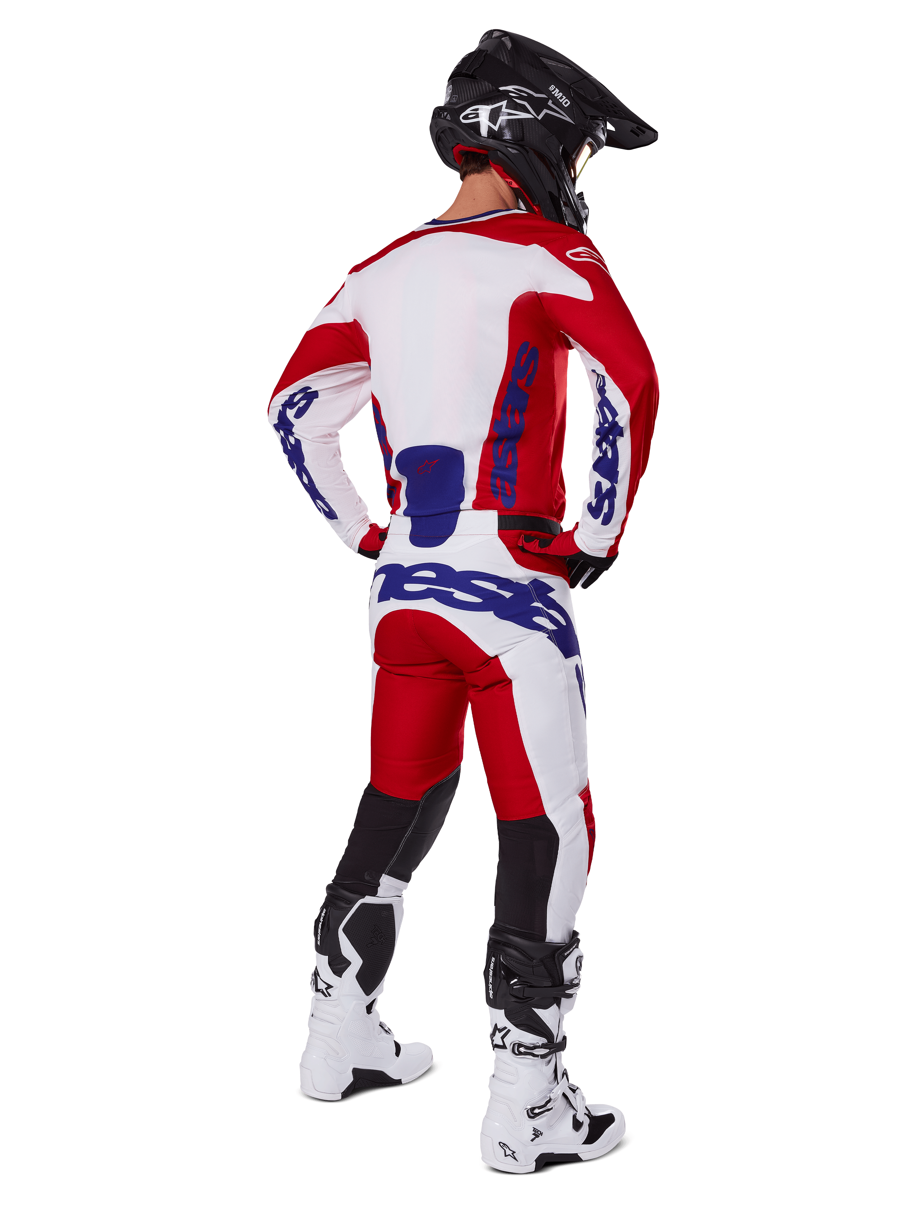Piloto de motocross visto de costas a usar a camisola e calças Alpinestars 2025 Racer Veil em vermelho e branco, com logótipos azuis, capacete preto e botas brancas, conjunto de equipamento completo para corridas todo-o-terreno
