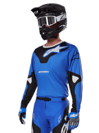 Alpinestars 2025 Racer Veil Gear Set, Blue Motocross Jersey with black and white graphics, worn with matching pants, black helmet, white goggles, and blue gloves, technical apparel for off-road racing