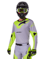 Piloto de motocross a usar o conjunto de equipamento Alpinestars Racer Veil 2025 em cinzento e verde néon, camisola e calças cinzento claro com painéis vibrantes em amarelo-verde néon e logótipos Alpinestars pretos, coordenado com luvas a condizer e capacete preto com óculos verde néon, vestuário profissional de corrida todo-o-terreno