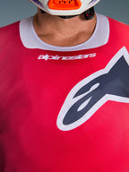 Grande plano da camisola Alpinestars Racer Portl 2026 em vermelho, com gola elástica cinzenta clara com marca branca e um logótipo Astars preto de grandes dimensões no peito, equipamento de motocross de alta performance