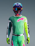 Alpinestars 2026 Racer Portl Jersey, camisola de motocross, verde, branco e preto com um grande logótipo Alpinestars rosa no peito, usada por um piloto com um capacete multicolorido vibrante e óculos a condizer, vestuário profissional de competição off-road