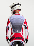 Alpinestars Techstar Maven, camisola de motocross para homem, vermelha e branca, vista traseira no piloto, tecido respirável com perfurações a laser
