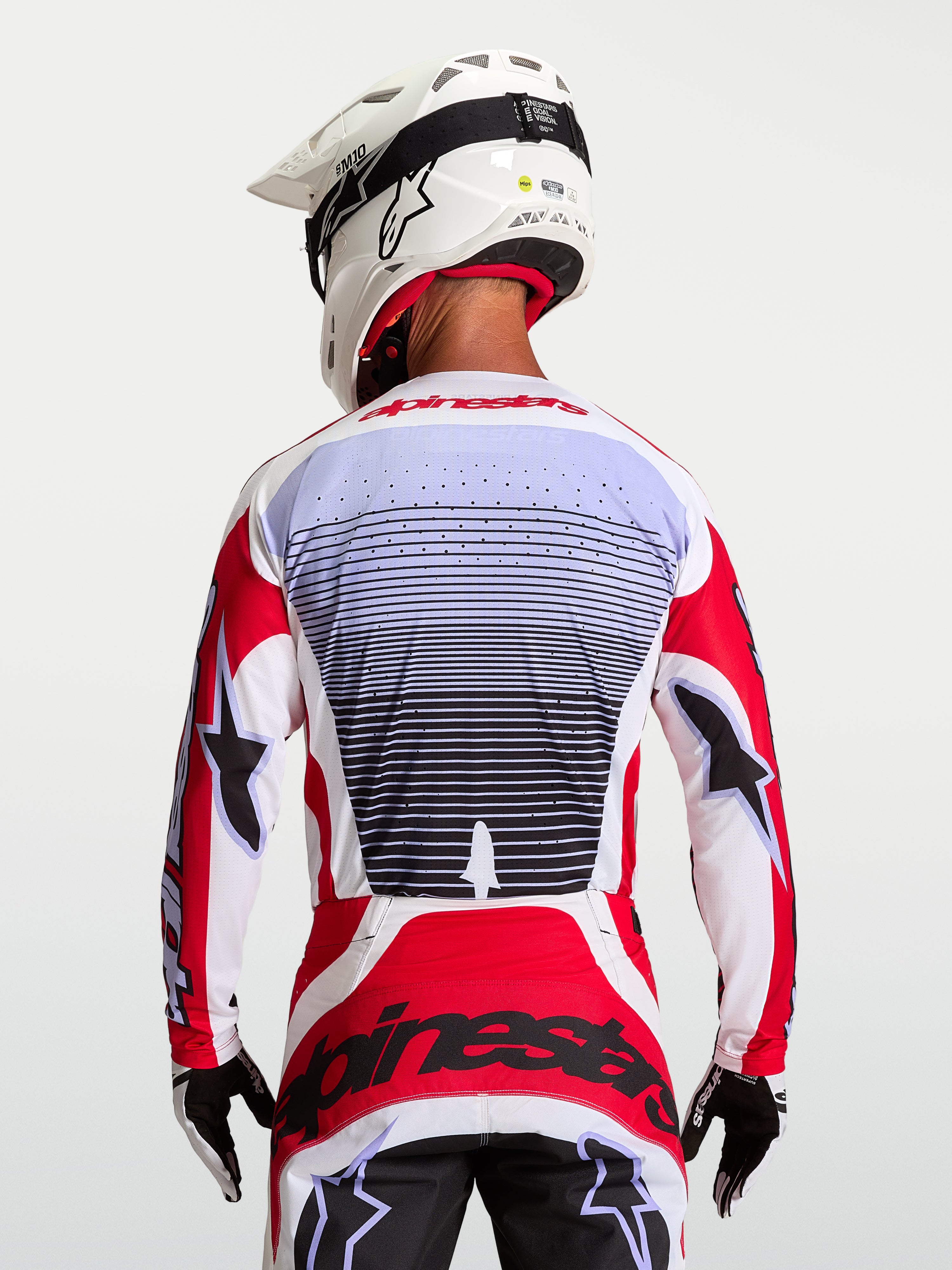 Alpinestars Techstar Maven, camisola de motocross para homem, vermelha e branca, vista traseira no piloto, tecido respirável com perfurações a laser