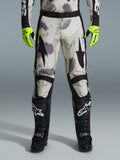 Alpinestars 2026 Racer Lahnd Pants, calças de motocross, padrão Sand Camo com grafismos abstratos em cinzento e roxo, usadas com luvas amarelo néon e botas pretas, com logótipos de estrela pretos nas coxas e cinto preto, equipamento de corrida off-road durável
