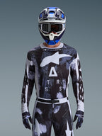 Piloto de motocross a usar o Conjunto de Equipamento Alpinestars Racer Lahnd 2026, camisola com padrão camuflado abstrato em preto e branco com logótipos brancos grandes e a inscrição "ATRS", calças e luvas a combinar, capacete azul e branco com óculos, conjunto de corrida de alta performance para motocross todo-o-terreno