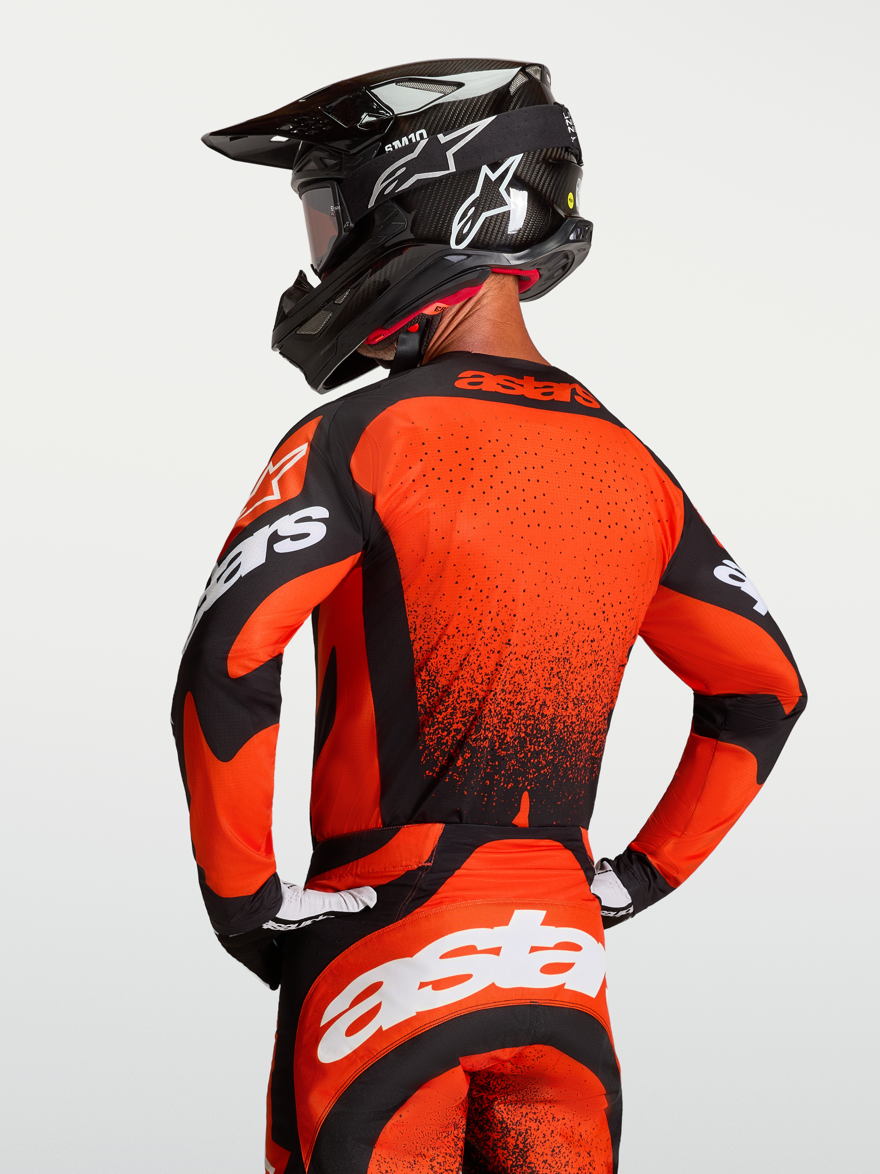 Alpinestars Camisola Techstar Swan, camisola de motocross para homem, vermelha e preta, vista traseira num modelo com capacete, ajuste de corrida e ventilação a laser