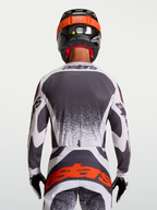 Alpinestars Camisola Techstar Swan, vista traseira de piloto de motocross, cinzenta e branca, com ventilação a laser.