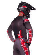 Alpinestars 2025 Supertech Lipan Gear Set, Motocross rider viewed from the back, charcoal grey jersey and pants with vibrant red 'astars' branding on the sleeves and back, paired with a black helmet
