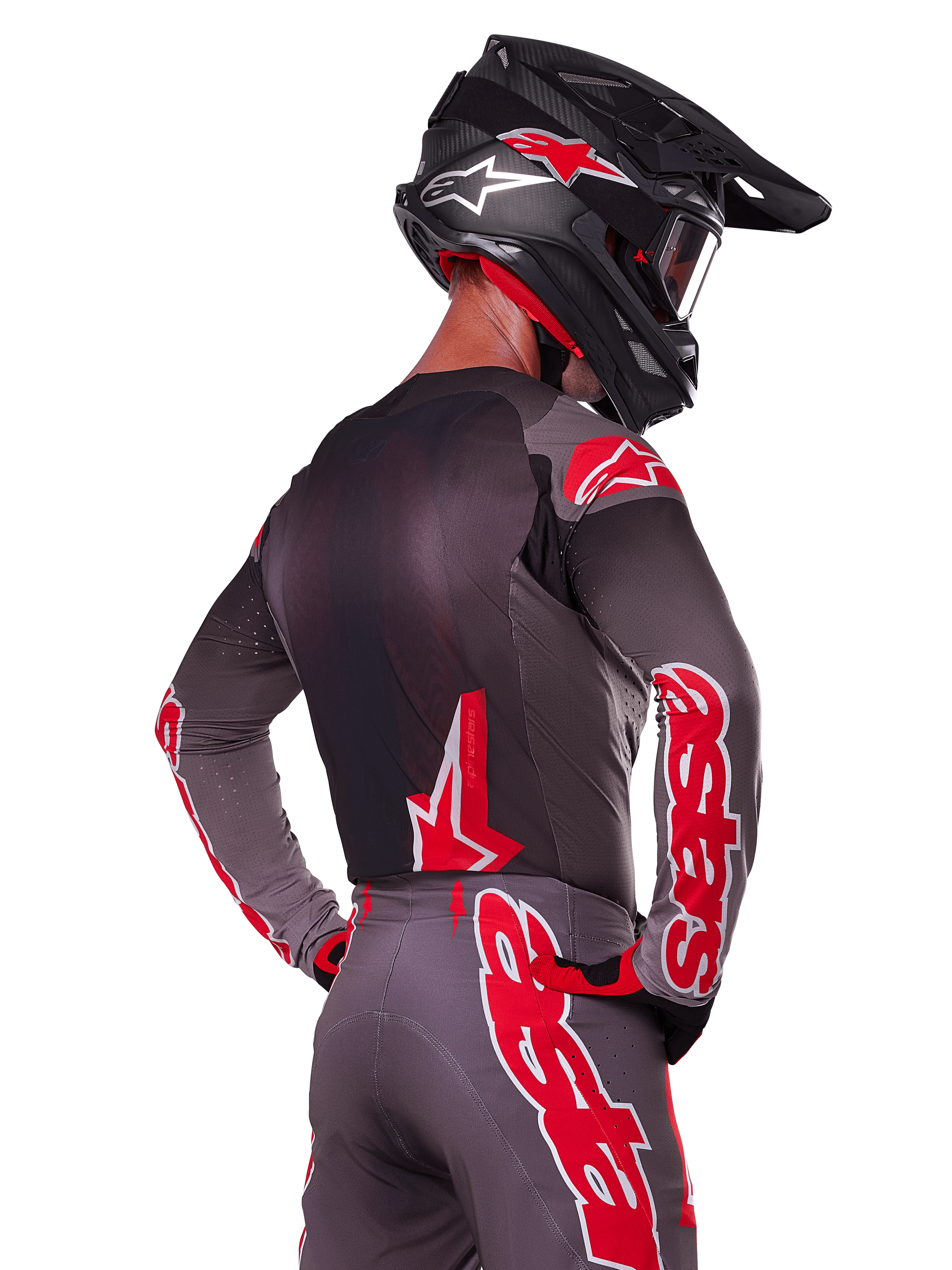 Alpinestars 2025 Supertech Lipan Gear Set, Motocross rider viewed from the back, charcoal grey jersey and pants with vibrant red 'astars' branding on the sleeves and back, paired with a black helmet