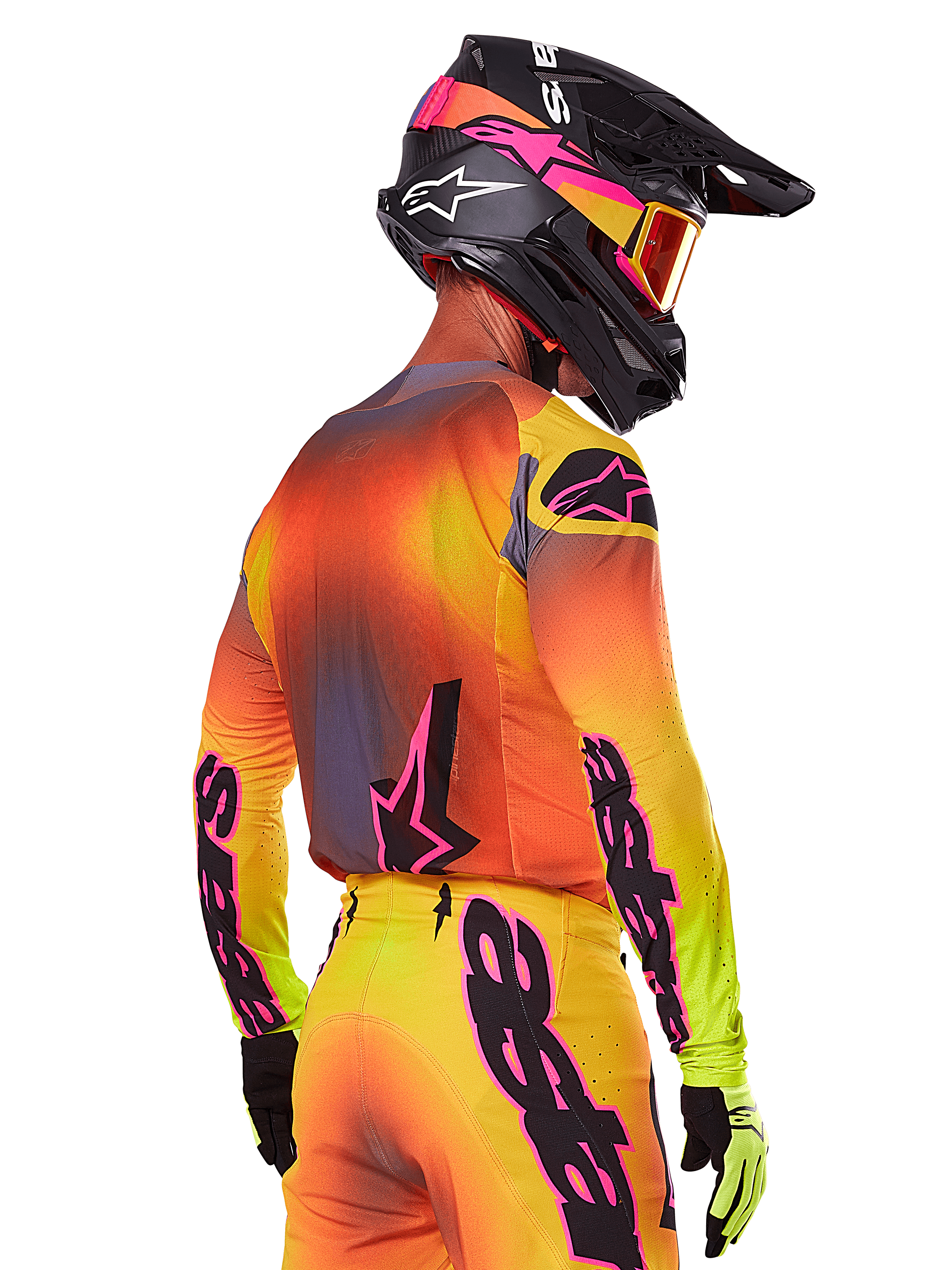 Piloto de motocross, visto de uma perspetiva lateral traseira, a usar o Conjunto de Equipamento Alpinestars Supertech Lipan 2025, com um gradiente de amarelo, laranja e vermelho, logótipos em preto e cor-de-rosa, capacete preto com detalhes rosa e óculos laranja, vestuário profissional de corrida todo-o-terreno