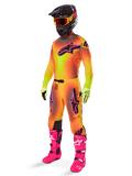 Piloto de motocross a usar o conjunto de equipamento Alpinestars Supertech Lipan 2025, camisola e calças com gradiente amarelo e laranja e detalhes cor-de-rosa, capacete preto com óculos amarelos e vermelhos, luvas amarelo brilhante e botas cor-de-rosa vibrante, conjunto de corrida todo-o-terreno coordenado