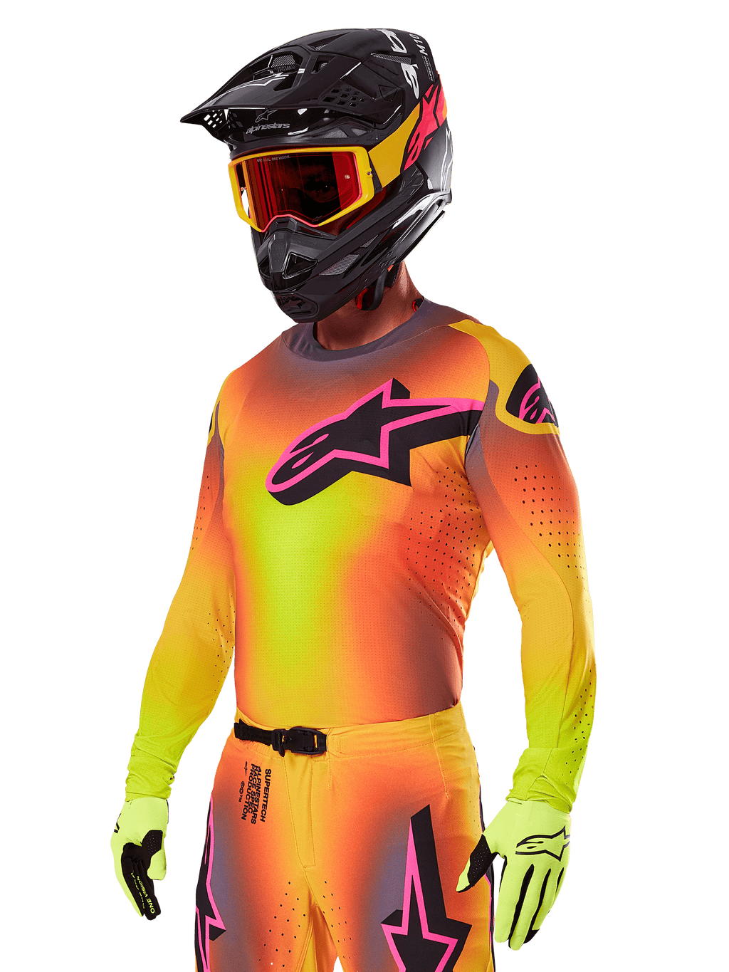 Piloto de motocross a usar o conjunto de equipamento Alpinestars 2025 Supertech Lipan, com uma camisola em gradiente amarelo e laranja com o logótipo Astars em cor-de-rosa e preto, luvas amarelo néon e capacete preto com óculos vermelhos, equipamento profissional de todo-o-terreno