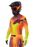 Piloto de motocross a usar o conjunto de equipamento Alpinestars 2025 Supertech Lipan, com uma camisola em gradiente amarelo e laranja com o logótipo Astars em cor-de-rosa e preto, luvas amarelo néon e capacete preto com óculos vermelhos, equipamento profissional de todo-o-terreno