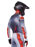 Piloto de motocross visto de costas a usar a camisola e o conjunto de equipamento Alpinestars Supertech Lipan 2025, cinzento com detalhes Orange Fluo, com logótipos destacados nas costas e mangas, capacete preto e luvas pretas, conjunto de corrida de motocross coordenado
