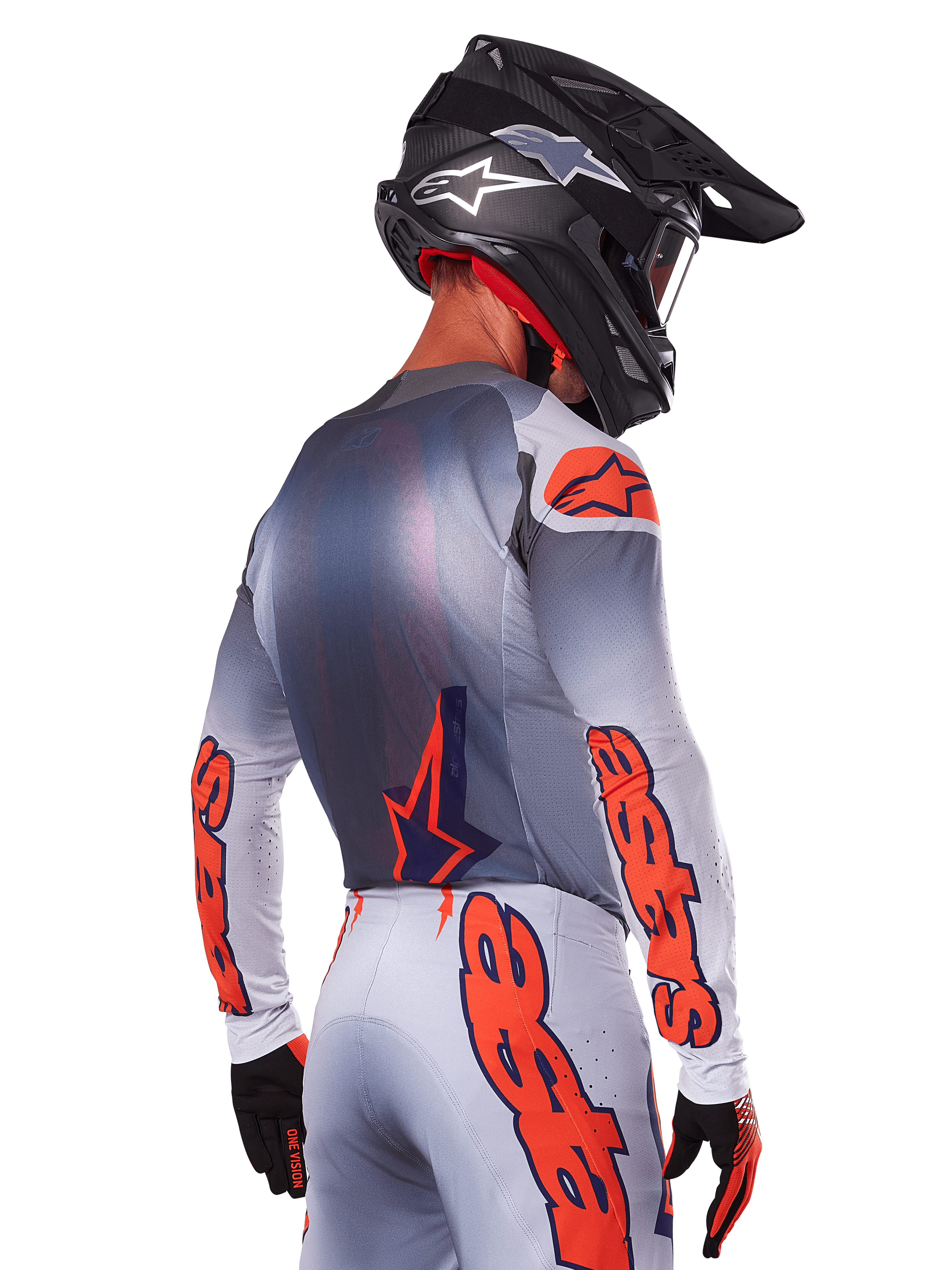 Piloto de motocross visto de costas a usar a camisola e o conjunto de equipamento Alpinestars Supertech Lipan 2025, cinzento com detalhes Orange Fluo, com logótipos destacados nas costas e mangas, capacete preto e luvas pretas, conjunto de corrida de motocross coordenado