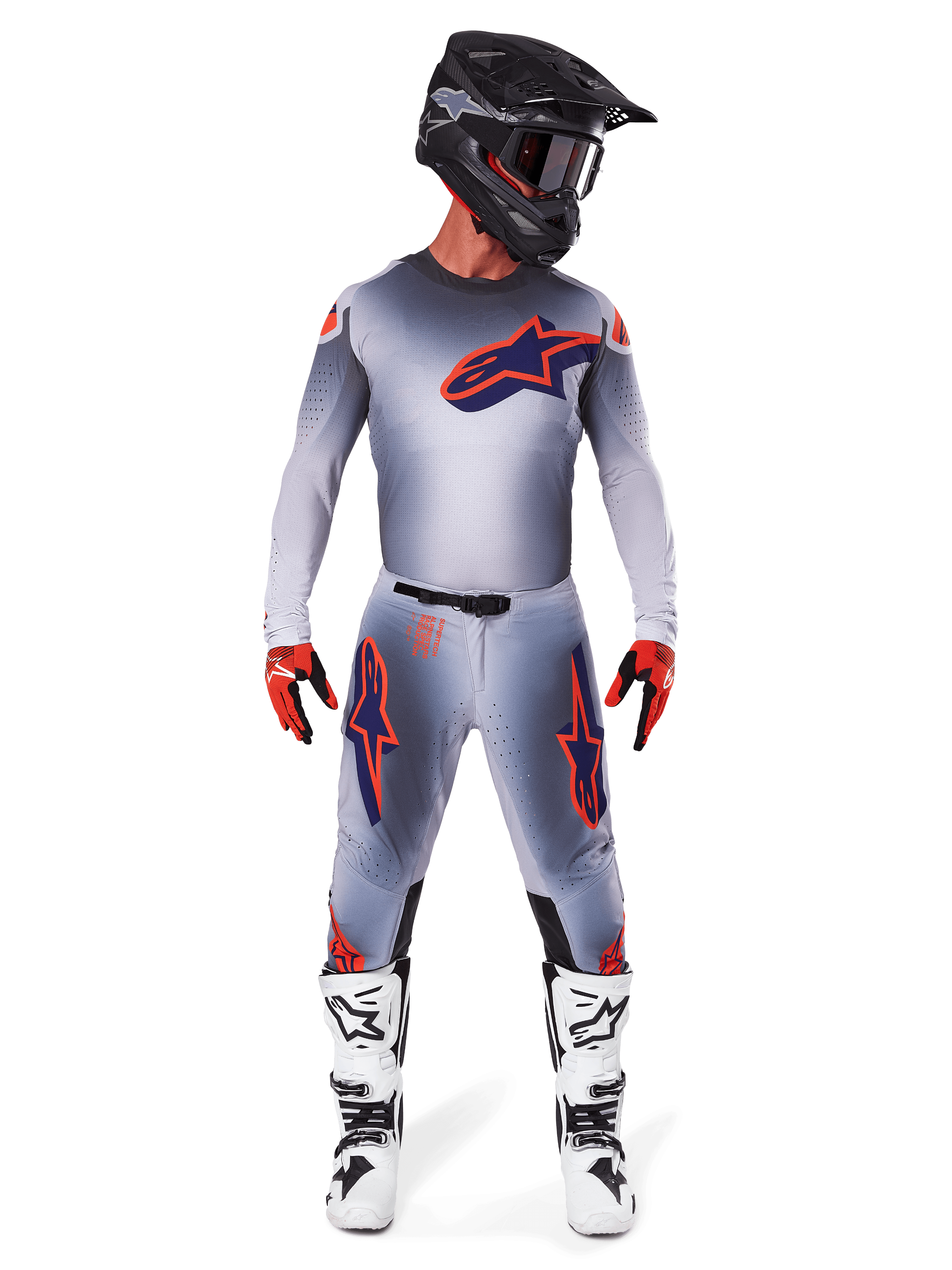 Piloto de motocross a usar o conjunto de equipamento Alpinestars Supertech Lipan 2025 em cinzento e laranja fluorescente, composto por camisola cinzenta com detalhes laranja e logótipo azul-marinho, calças cinzentas com logótipos grandes, capacete preto mate, botas brancas e pretas, e luvas vermelhas e pretas, equipamento de corrida de nível profissional.
