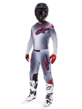 Alpinestars 2025 Supertech Lipan Gear Set, equipamento de motocross, cinzento com grafismos de estrelas em laranja fluo e azul marinho, usado com capacete preto, luvas vermelhas e pretas e botas brancas e pretas, fato profissional de off-road completo com design ventilado