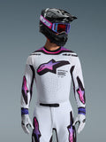 Piloto de motocross a usar a camisola 2026 Supertech AFD Vista em branco, roxo e preto, capacete preto com detalhes cor-de-rosa, óculos roxos e luvas brancas, equipamento de corte atlético para performance profissional em todo-o-terreno