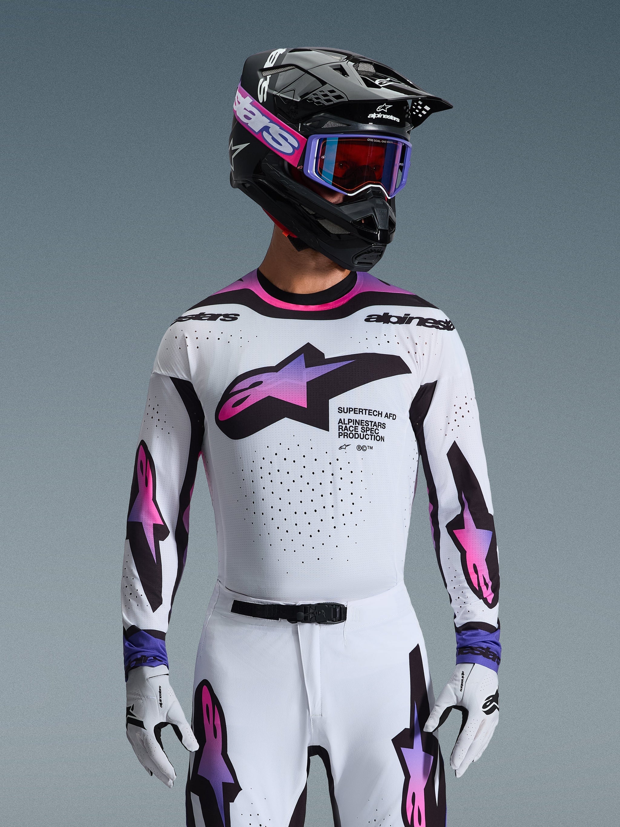 Motocross rider wearing the 2026 Supertech AFD Vista Jersey in White Purple and Black, featuring a black helmet with pink branding, purple goggles, and matching white gloves, athletic fit gear designed for professional off-road racing performance