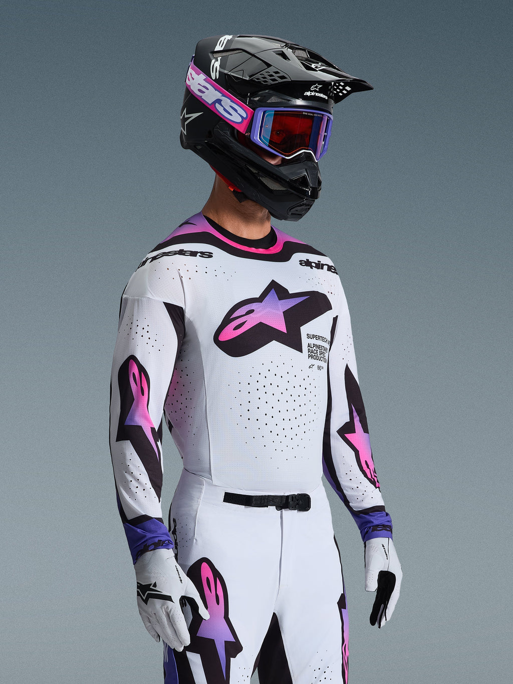 Piloto de motocross a usar a Camisola 2026 Supertech AFD Vista em Branco Roxo e Preto, calças brancas e roxas a condizer, capacete preto com óculos roxos e luvas brancas, equipamento profissional completo de corridas todo-o-terreno.
