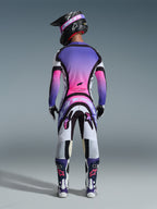 Rear view of a motocross rider wearing the Alpinestars 2026 Supertech AFD Vista Gear Set, jersey and pants featuring a vibrant white, purple, and pink gradient with black accents, black helmet with purple goggles, matching purple and white boots, coordinated professional racing outfit for off-road performance.