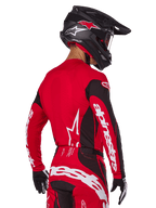 Piloto de motocross visto de costas a usar o conjunto de equipamento Alpinestars 2025 Techstar Dreem, camisola vermelha e preta com logótipo branco nas mangas, calças vermelhas e pretas condizentes com logótipo branco no assento, capacete de carbono preto com detalhes vermelhos, luvas pretas e brancas, equipamento de corrida profissional para todo-o-terreno