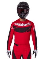 Alpinestars 2025 Techstar Dreem Jersey, equipamento de motocross, vermelho vivo e preto, com o logótipo 'astars' branco e painel de ventilação preto no peito, usado com calças a condizer, capacete preto e luvas brancas e pretas, concebido para competição profissional de todo-o-terreno