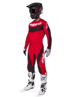 Vista de corpo inteiro de um piloto de motocross com o conjunto de equipamento Techstar Dreem 2025 em vermelho brilhante e preto, composto por camisola de performance com logótipo branco, calças ripstop elásticas a condizer, capacete preto com viseira vermelha, luvas brancas e pretas e botas Tech brancas, fato de corrida especializado para competição todo-o-terreno.