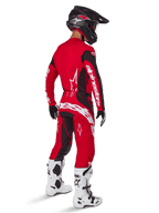 Piloto de motocross a usar o conjunto de equipamento Alpinestars Techstar Dreem 2025 em Vermelho Vivo e Preto, com logótipos brancos na camisola e nas calças, combinado com um capacete preto, botas brancas e pretas, e luvas pretas e brancas, vista traseira de três quartos.
