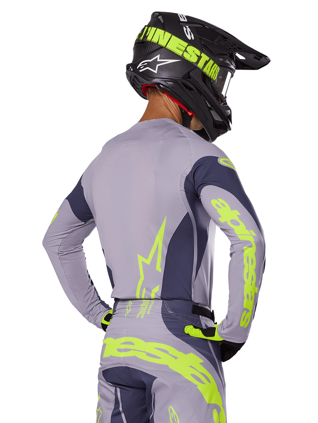 Piloto de motocross visto de costas a usar o conjunto de equipamento Alpinestars 2025 Techstar Dreem, camisola e calças cinzentas com logótipos em amarelo-verde néon vibrante, capacete preto a condizer com grafismos néon, equipamento de corrida de motocross profissional