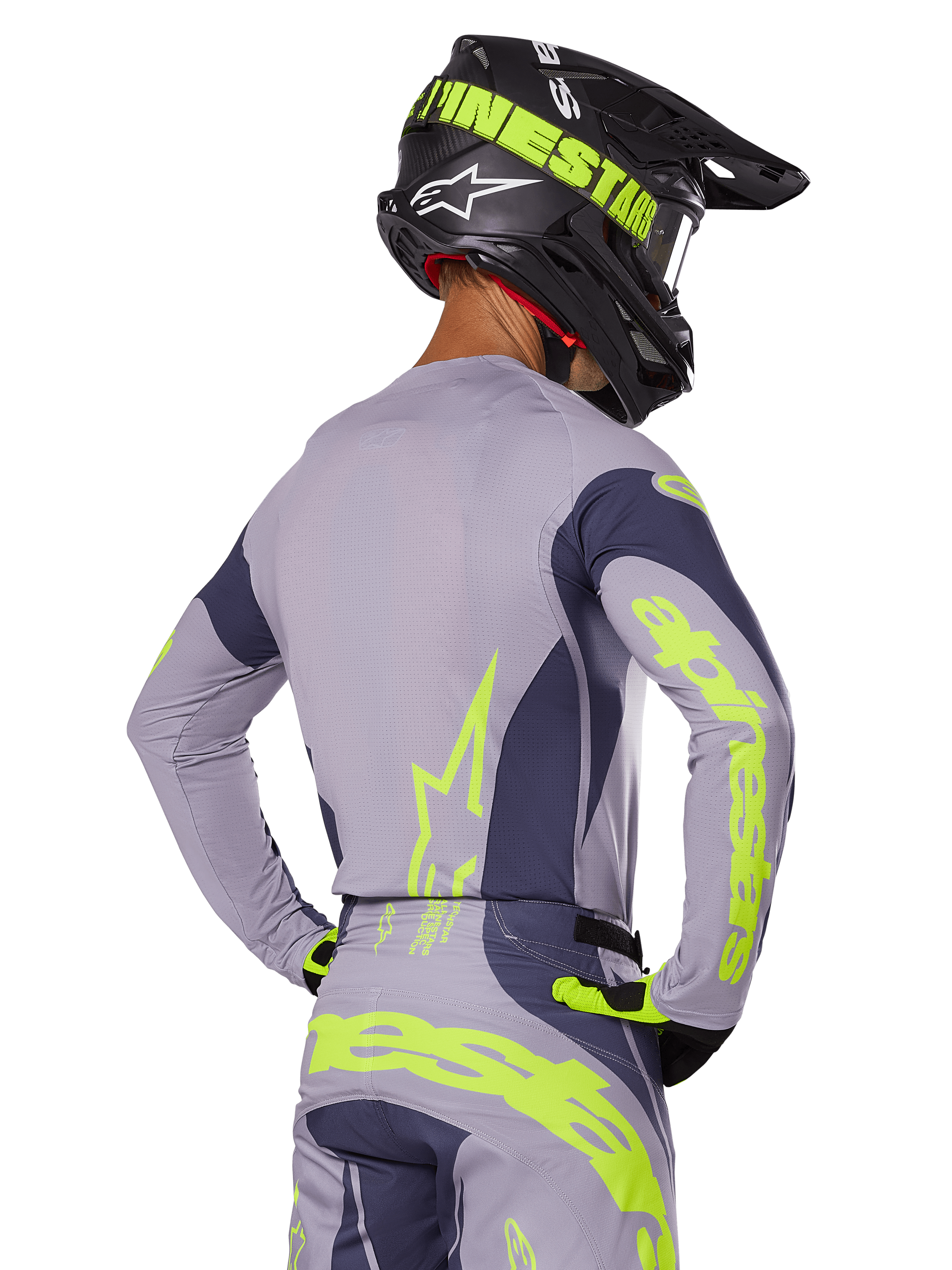 Piloto de motocross visto de costas a usar o conjunto de equipamento Alpinestars 2025 Techstar Dreem, camisola e calças cinzentas com logótipos em amarelo-verde néon vibrante, capacete preto a condizer com grafismos néon, equipamento de corrida de motocross profissional