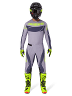Piloto de motocross a usar o conjunto de equipamento Alpinestars Techstar Dreem 2025 em cinzento e cinzento escuro com detalhes em amarelo néon, incluindo camisola, calças, botas amarelo néon e capacete preto, concebido para competição profissional de todo-o-terreno.