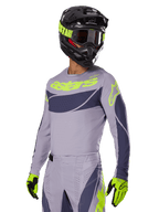 Piloto de motocross a usar a camisola Alpinestars 2025 Techstar Dreem em cinzento e cinzento escuro, com logótipo 'astars' em amarelo néon no peito, combinada com capacete, óculos e luvas a condizer para um visual coordenado de corrida todo-o-terreno