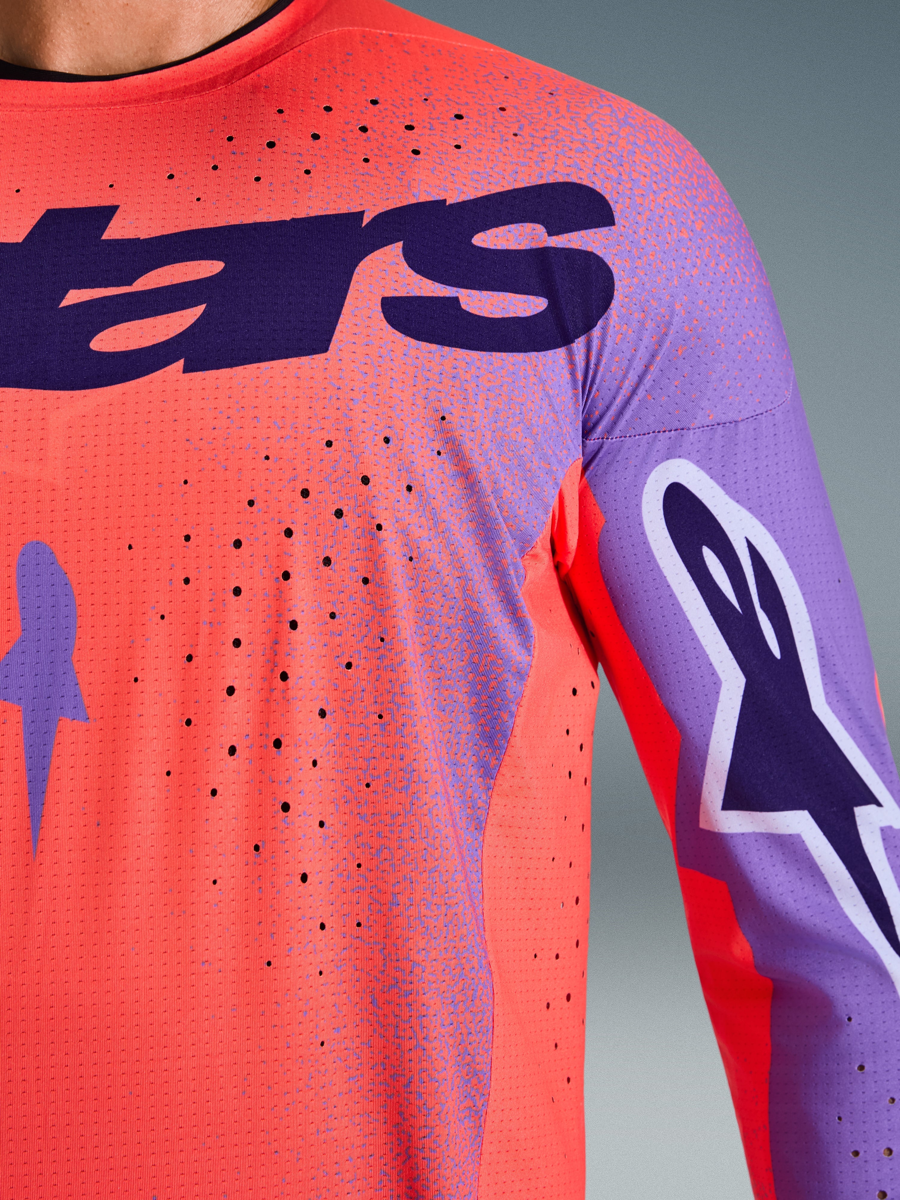 Alpinestars 2026 Supertech Scenz Jersey, camisola de motocross, Hot Coral e roxo, vista aproximada da textura de malha respirável e perfurações cortadas a laser, com logótipo grande no peito e grafismos nas mangas, para corridas profissionais de todo-o-terreno.