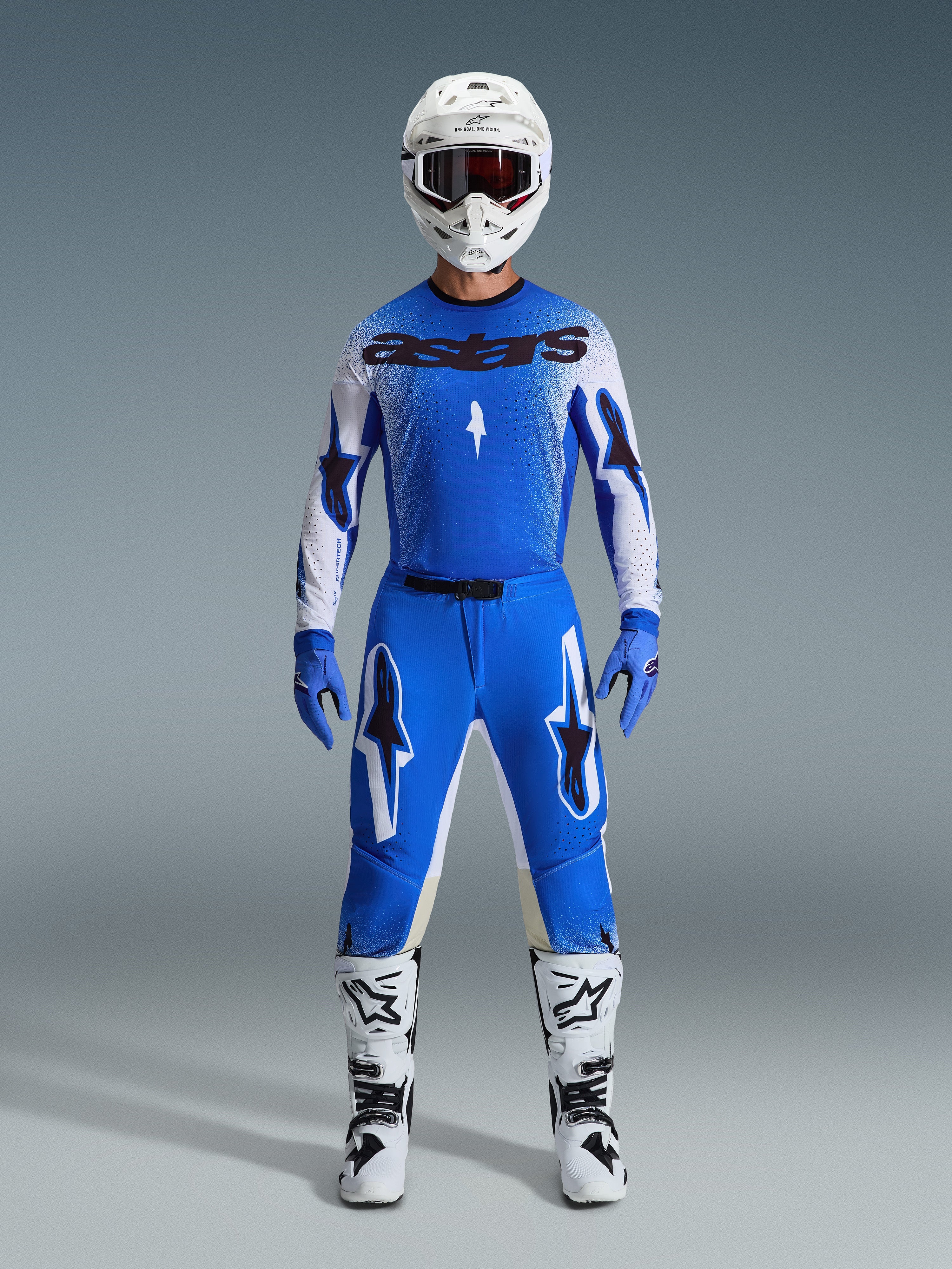 Motocross rider wearing the Alpinestars 2026 Supertech Scenz Gear Set in Ucla Blue and White, featuring a lightweight blue and white jersey with black branding, matching blue pants, white racing helmet, and white motocross boots, pro-level performance gear for off-road racing.