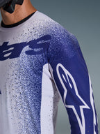 Grande plano da Camisola Alpinestars Supertech Scenz 2026 em cinzento claro e azul escuro, apresentando perfurações cortadas a laser, padrão gráfico salpicado, logótipo Astars branco na manga e corte de performance para motocross profissional.