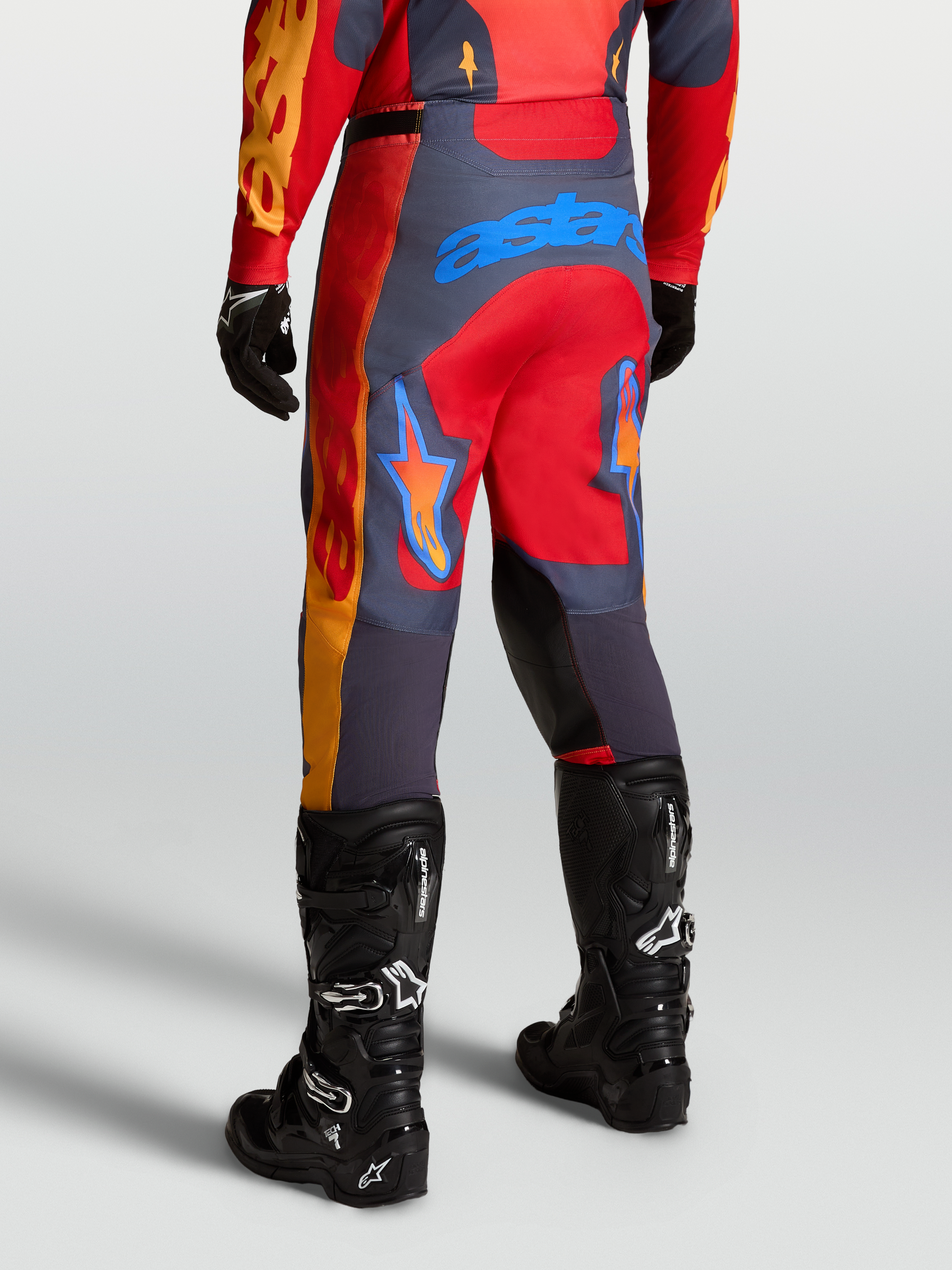 Alpinestars Calças Racer Hunt, calças de motocross para homem, vermelhas e cinzentas, vista traseira em posição de pilotagem off-road.
