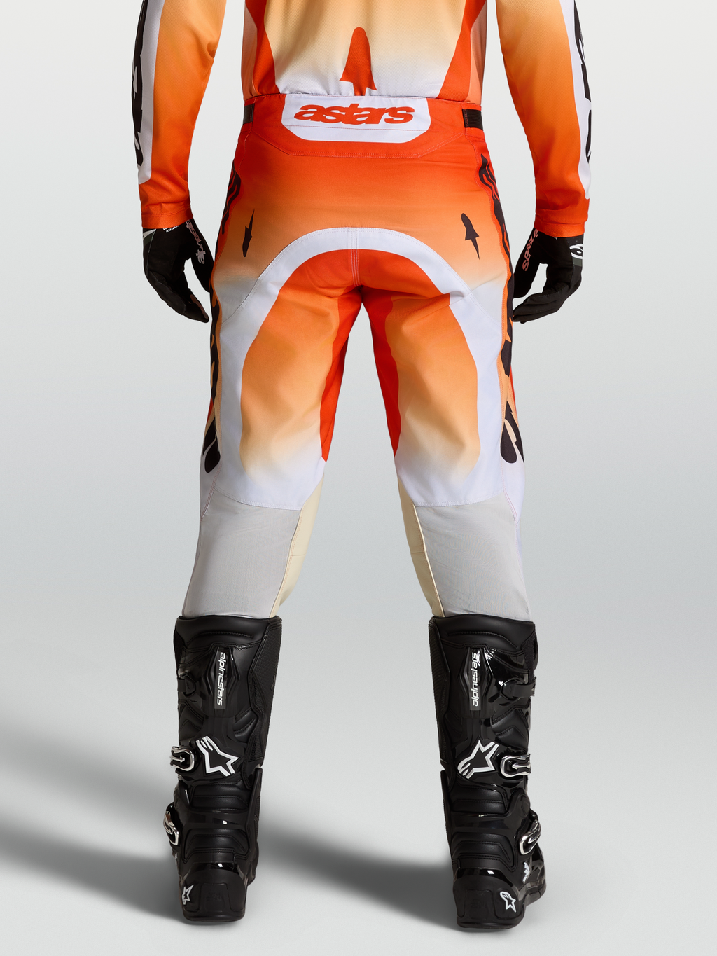 Alpinestars Calças Racer Amber, calças de motocross laranjas e brancas, ajuste de corrida, vista traseira no modelo com botas pretas