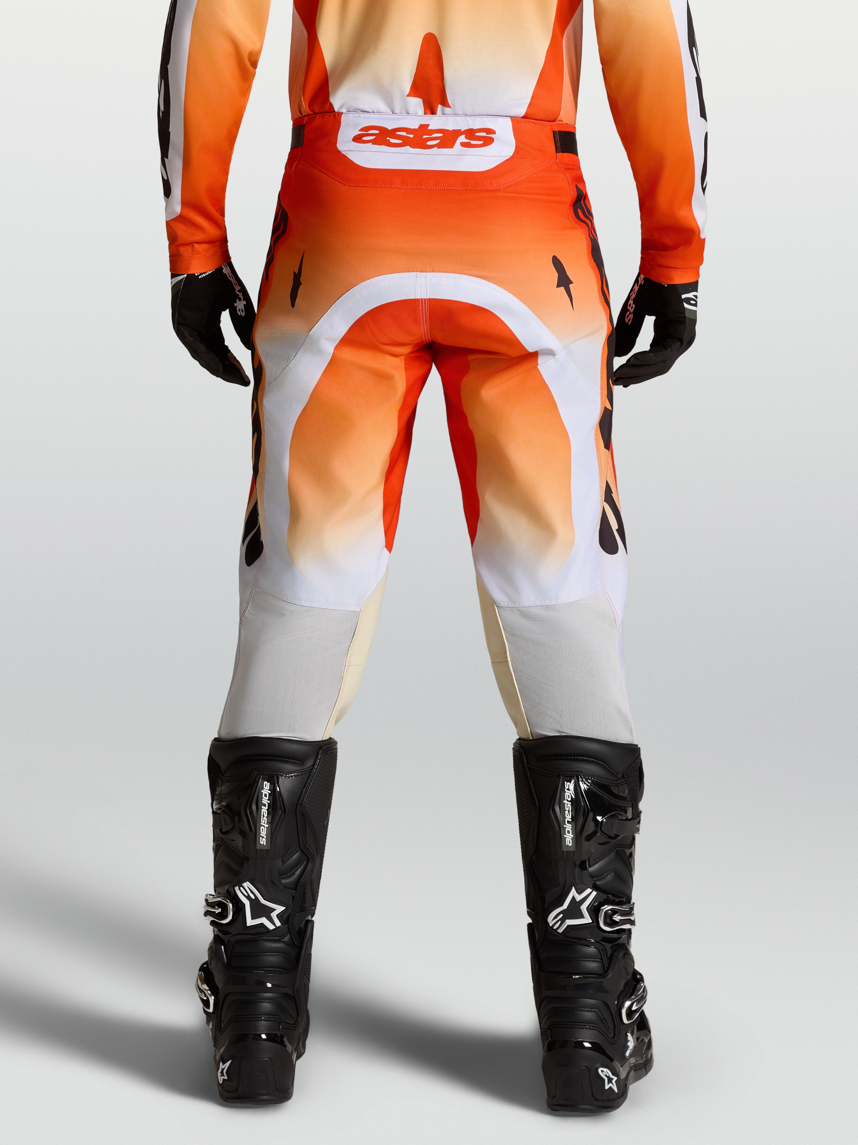 Alpinestars Calças Racer Amber, calças de motocross laranjas e brancas, ajuste de corrida, vista traseira no modelo com botas pretas