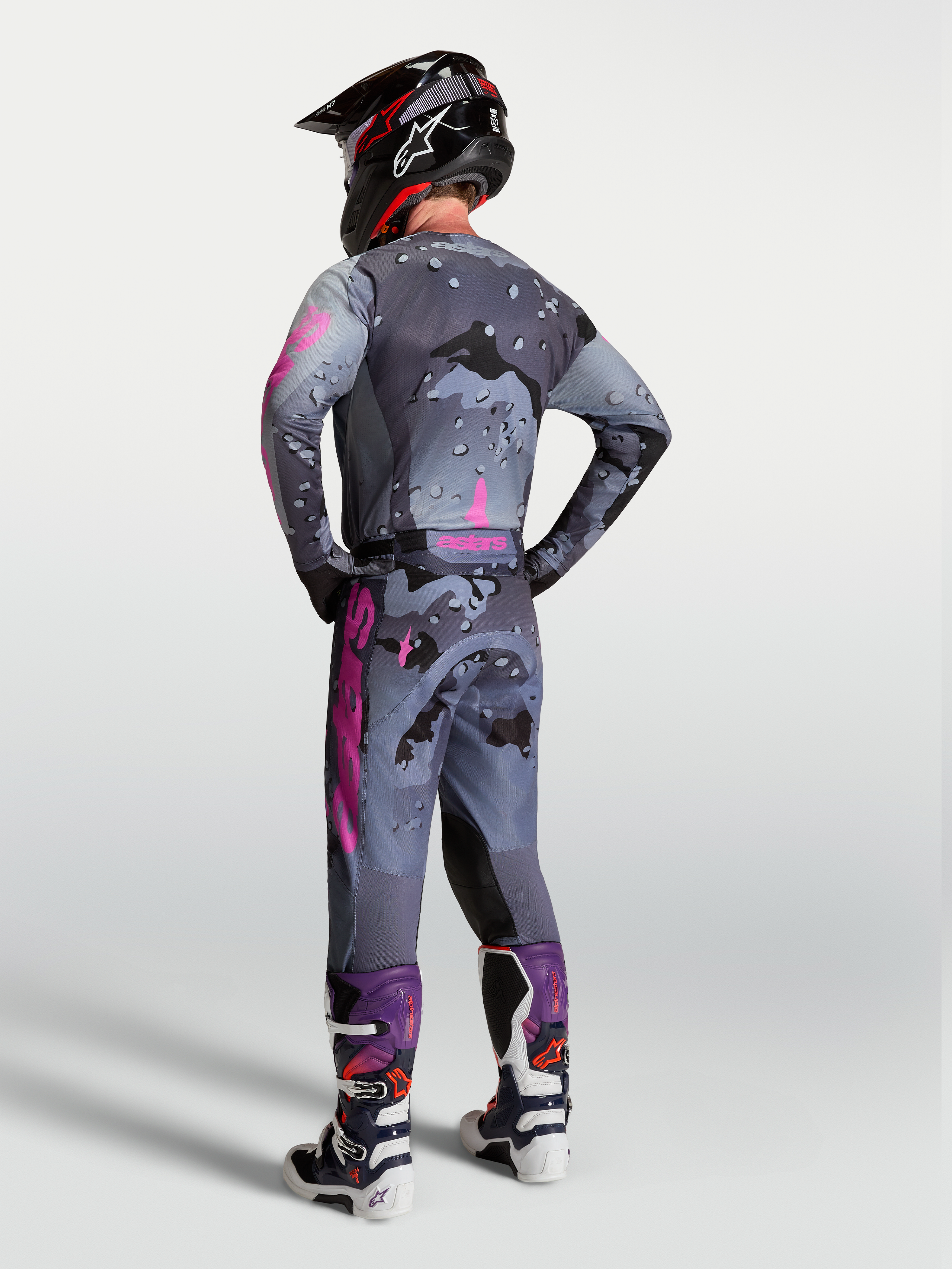 Alpinestars Racer Lone, calças de motocross para homem, cinzentas camufladas e roxas, vista traseira com camisola e botas.