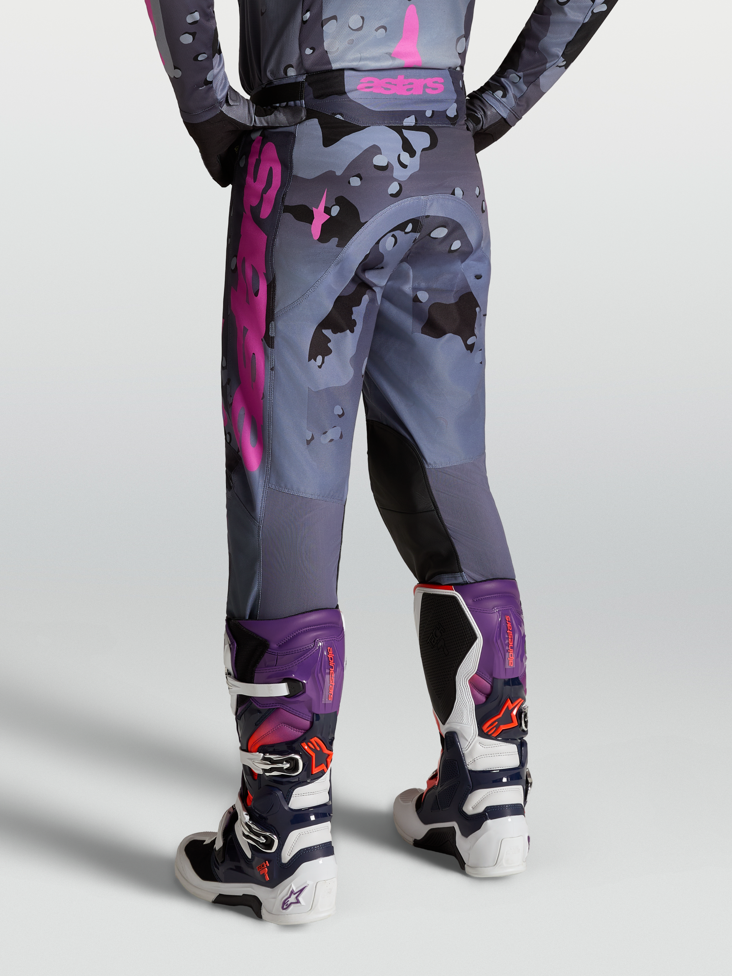 Alpinestars Calças Racer Lone, calças de motocross para homem em padrão camo cinzento e roxo, vista traseira com botas Tech 7.