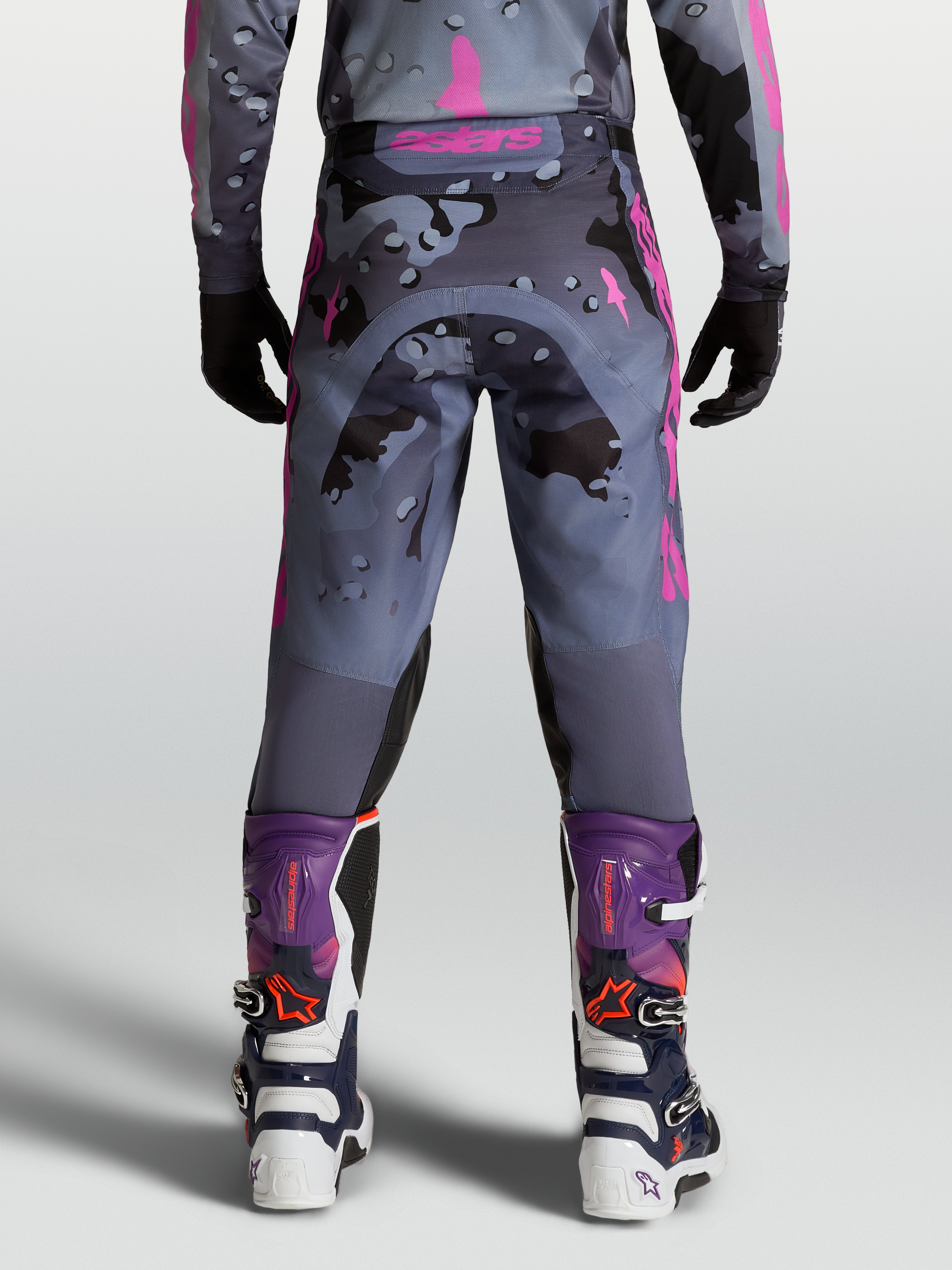 Alpinestars Calças Racer Lone, calças de motocross para homem, camuflagem cinzenta e roxa, vista traseira no modelo com botas MX a condizer