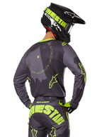 Piloto de motocross visto de costas a usar o Conjunto de Equipamento Racer Hollow 2025, camisola cinzenta com texto circular amarelo fluorescente e logótipos de estrela, calças cinzentas e amarelas a condizer com marca proeminente no assento, capacete preto e verde-lima, conjunto coordenado para corridas fora de estrada
