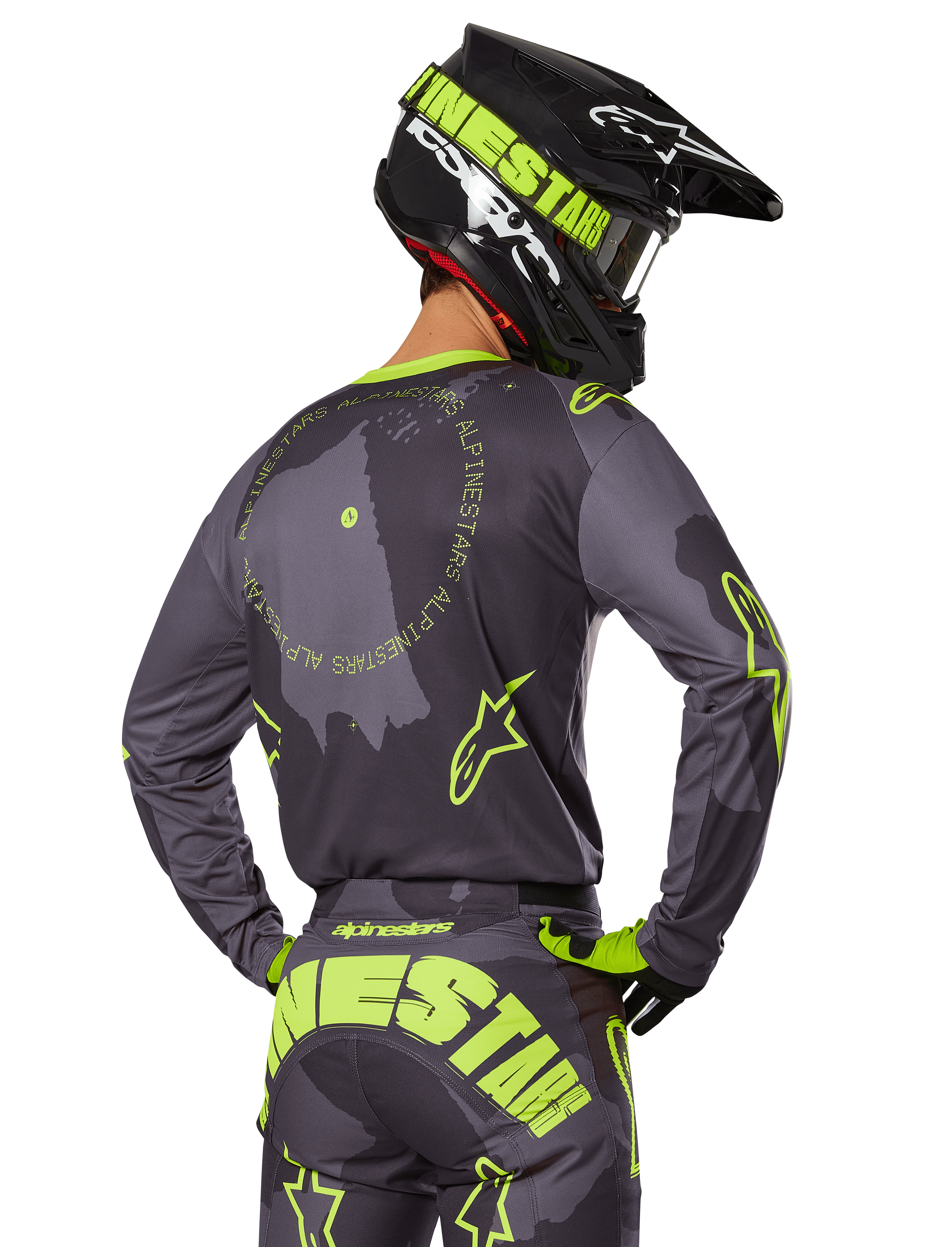 Piloto de motocross visto de costas a usar o Conjunto de Equipamento Racer Hollow 2025, camisola cinzenta com texto circular amarelo fluorescente e logótipos de estrela, calças cinzentas e amarelas a condizer com marca proeminente no assento, capacete preto e verde-lima, conjunto coordenado para corridas fora de estrada
