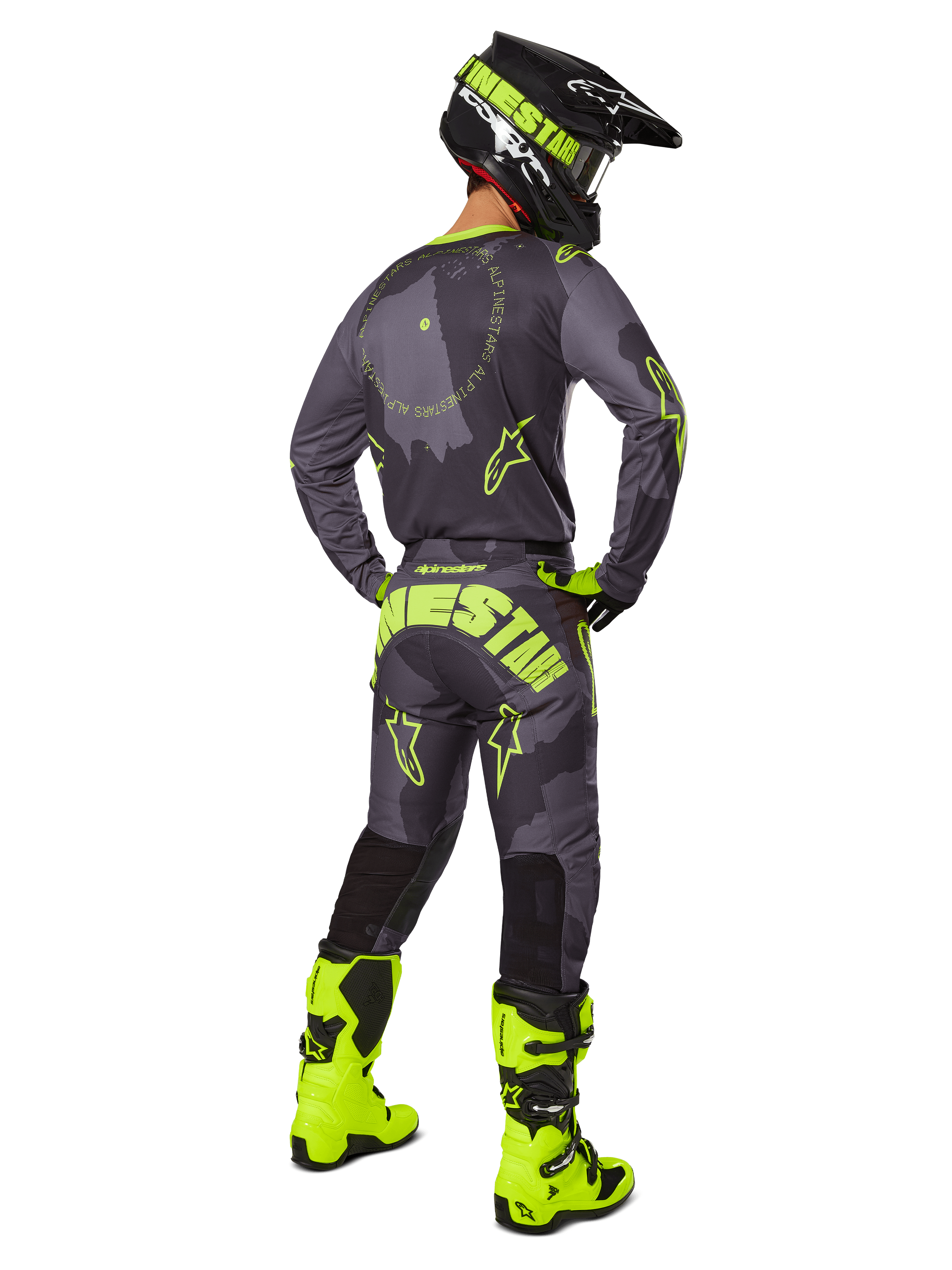 Vista traseira de um piloto de motocross a usar o conjunto de equipamento Racer Hollow 2025 em Dark Camo Yellow Fluo, com uma camisola camuflada cinzenta com detalhes em amarelo néon, calças de motocross a condizer com marca de destaque no assento, botas em amarelo néon brilhante e um capacete preto com óculos amarelos.