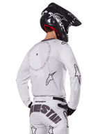 Motocross rider from the back wearing the Alpinestars 2025 Racer Hollow Gear Set in White, white long-sleeve jersey with grey star logos and circular graphics, matching white pants with bold branding on the seat, black helmet, coordinated off-road racing gear.