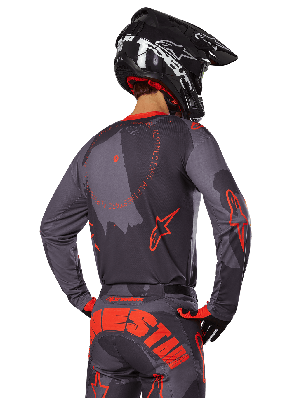 Alpinestars 2025 Racer Hollow Jersey, vista traseira de um piloto de motocross com equipamento em Cinzento Camuflado e Laranja Fluo, calças camufladas a condizer com letras Alpinestars grandes em laranja, capacete preto, design de vestuário profissional para todo-o-terreno