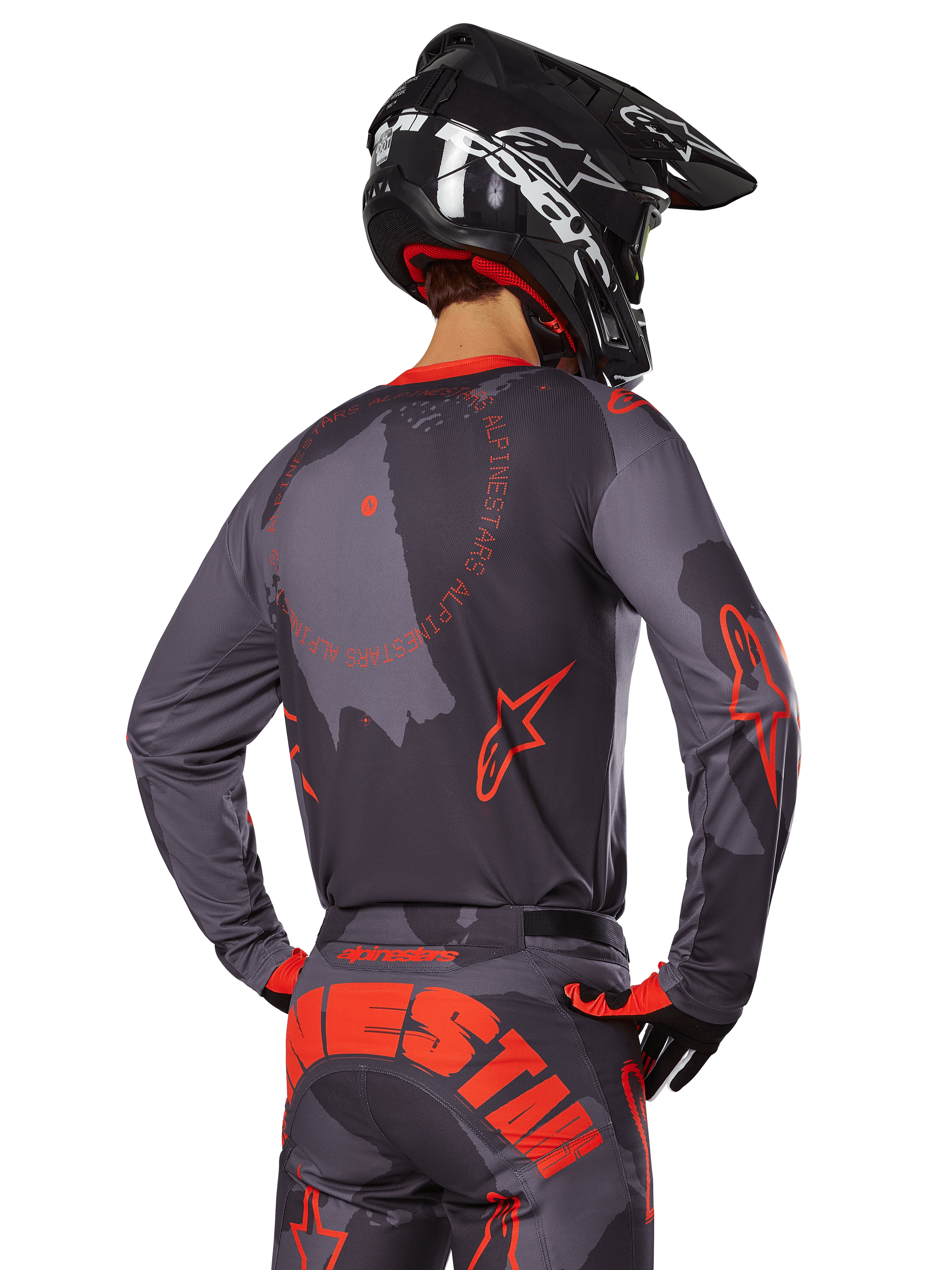 Alpinestars 2025 Racer Hollow Jersey, vista traseira de um piloto de motocross com equipamento em Cinzento Camuflado e Laranja Fluo, calças camufladas a condizer com letras Alpinestars grandes em laranja, capacete preto, design de vestuário profissional para todo-o-terreno