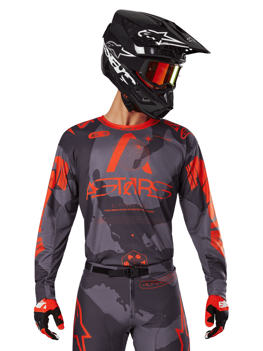 Alpinestars 2025 Racer Hollow Jersey, camisola de motocross, camuflado cinzento e laranja fluorescente, usada com conjunto de equipamento a condizer incluindo calças e luvas, com capacete preto com gráficos brancos e óculos, marca ASTARS em destaque, vestuário desportivo de proteção para motocross